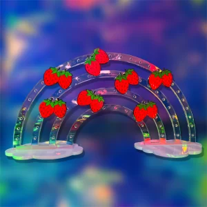 A colorful digital illustration of a semi-transparent rainbow decorated with bright red strawberries against a blurry blue and purple background.
