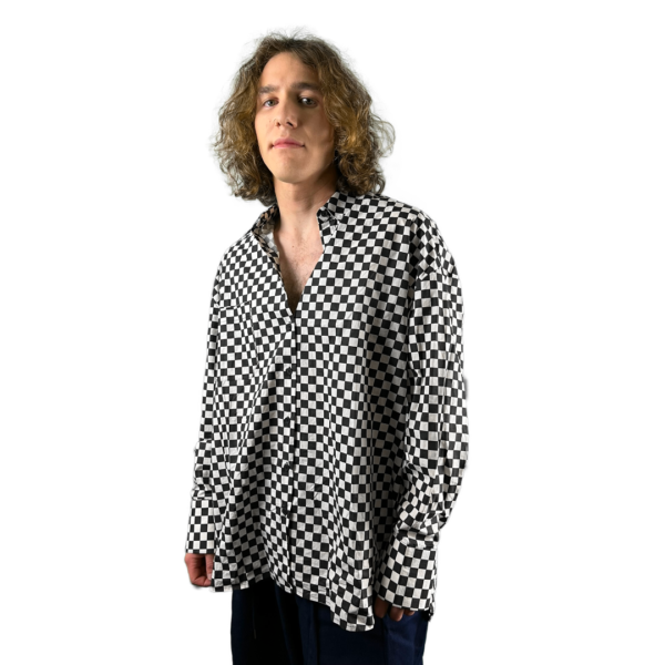 A person with shoulder-length curly hair wearing a checkered shirt, standing against a white background and looking directly at the camera.